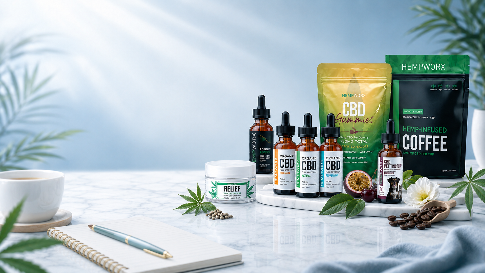 HempWorx CBD oil, gummies, Relief cream, hemp infused coffee and pet tincture arranged on marble beside a notebook and coffee